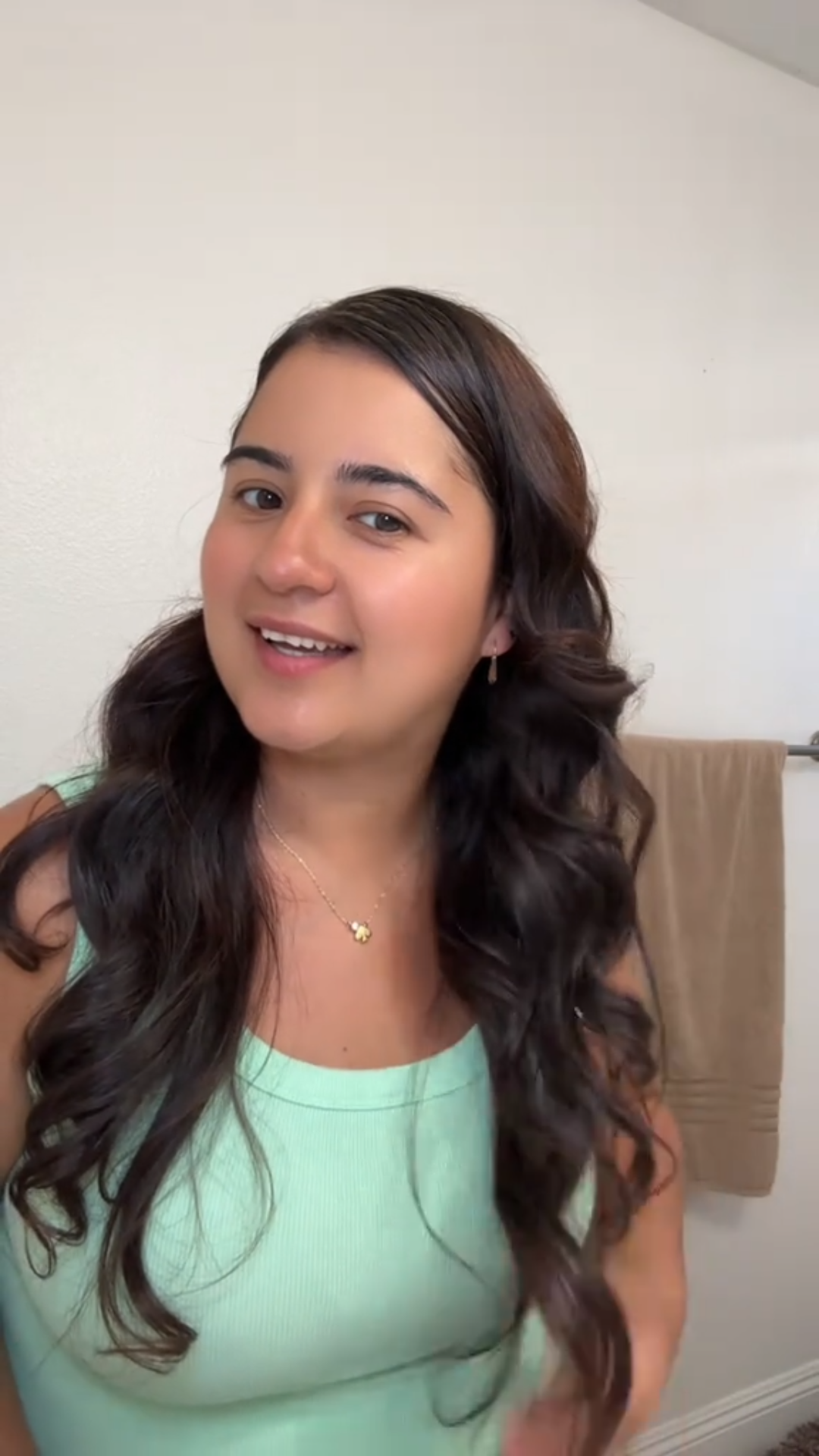 Woman with long, wavy hair wearing a light green top in a bathroom setting.